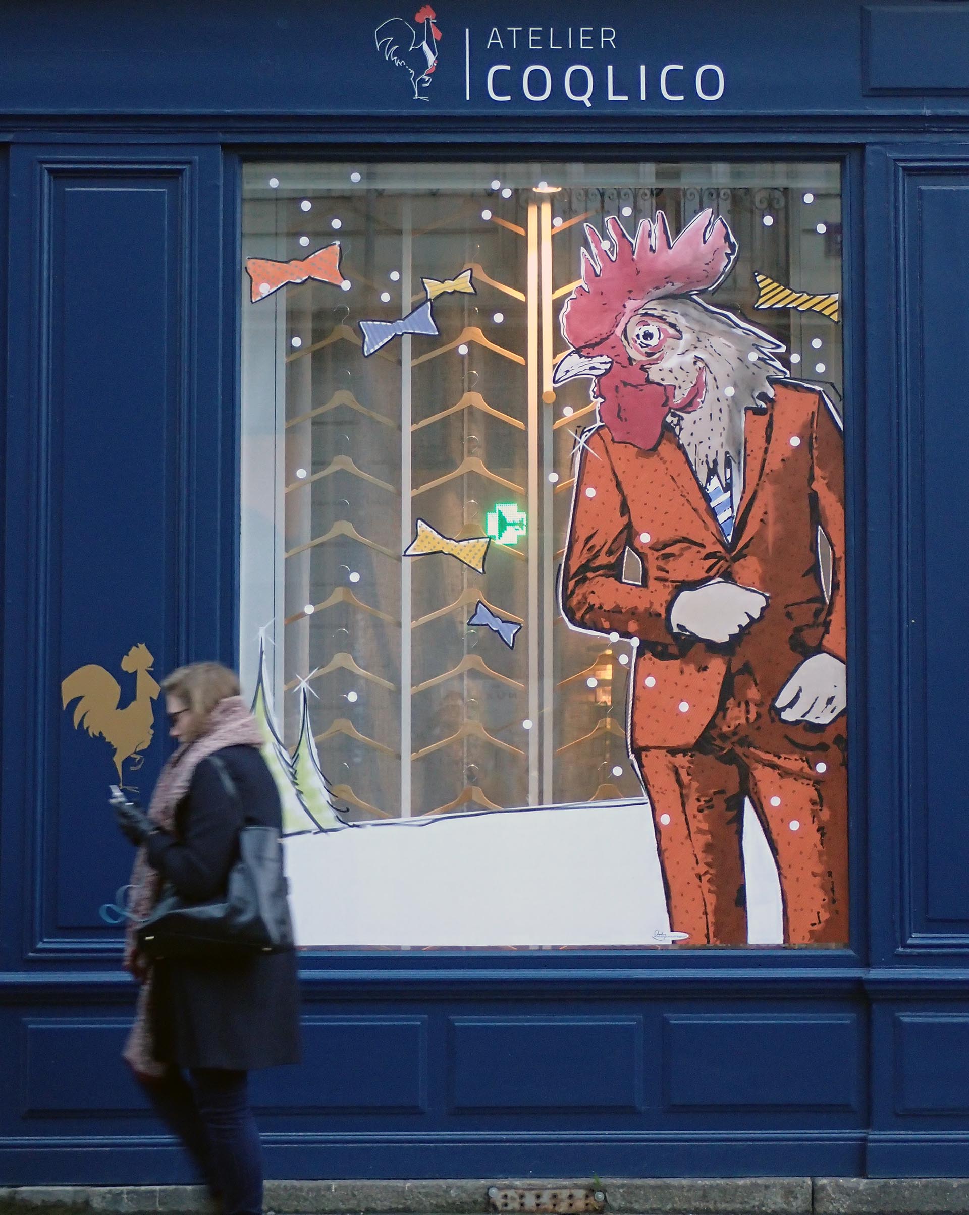 Décor de Noël peint sur la vitrine d’Atelier Coqlico avec coq élégant et sapins stylisés