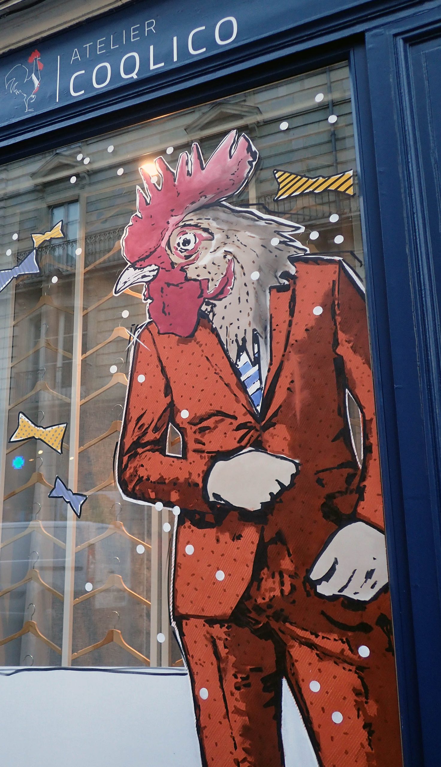 Décor de Noël peint sur la vitrine d’Atelier Coqlico avec coq élégant et sapins stylisés