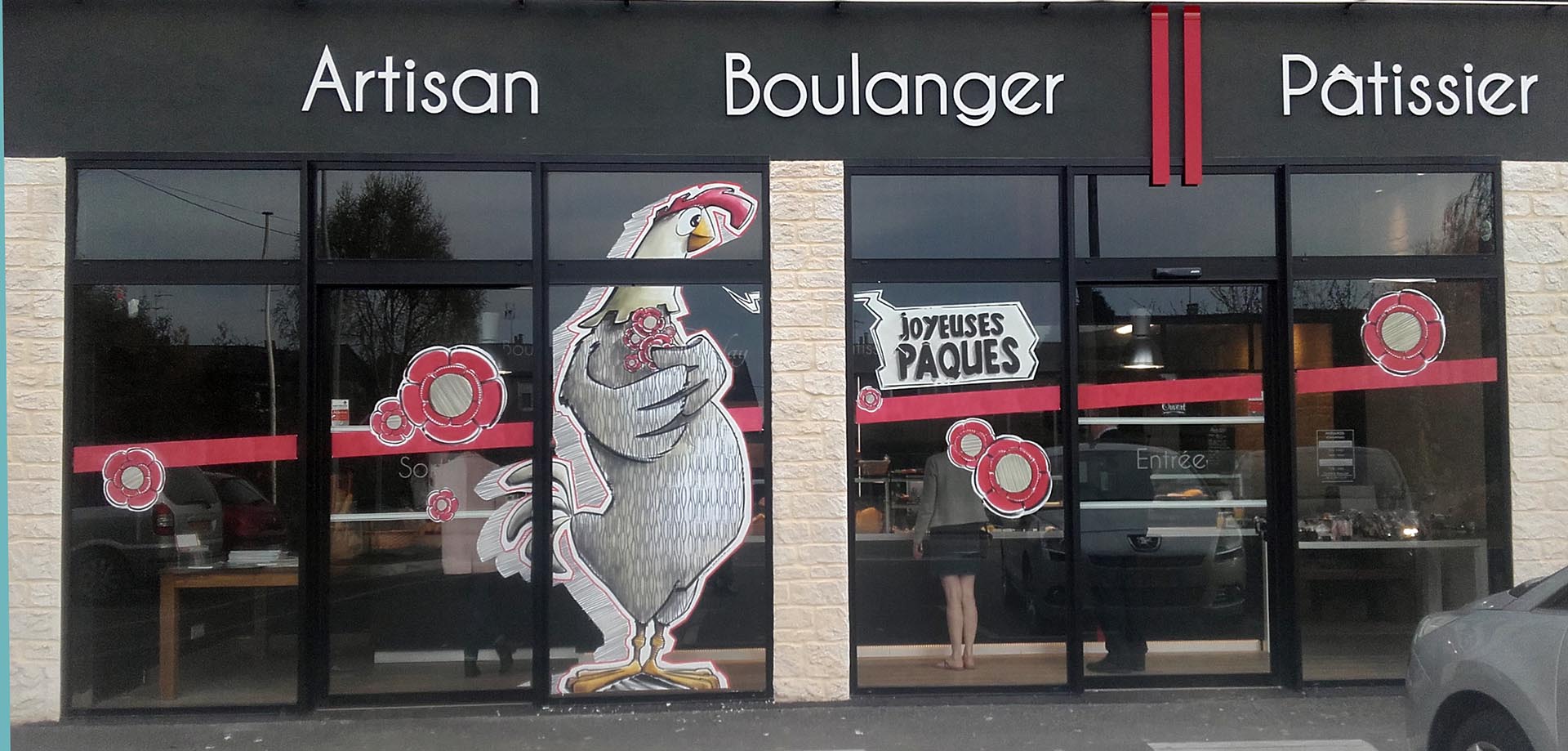 Peinture sur vitrine de Pâques par Jean‑Charles Varlet, poule stylisée et fleurs rouges.