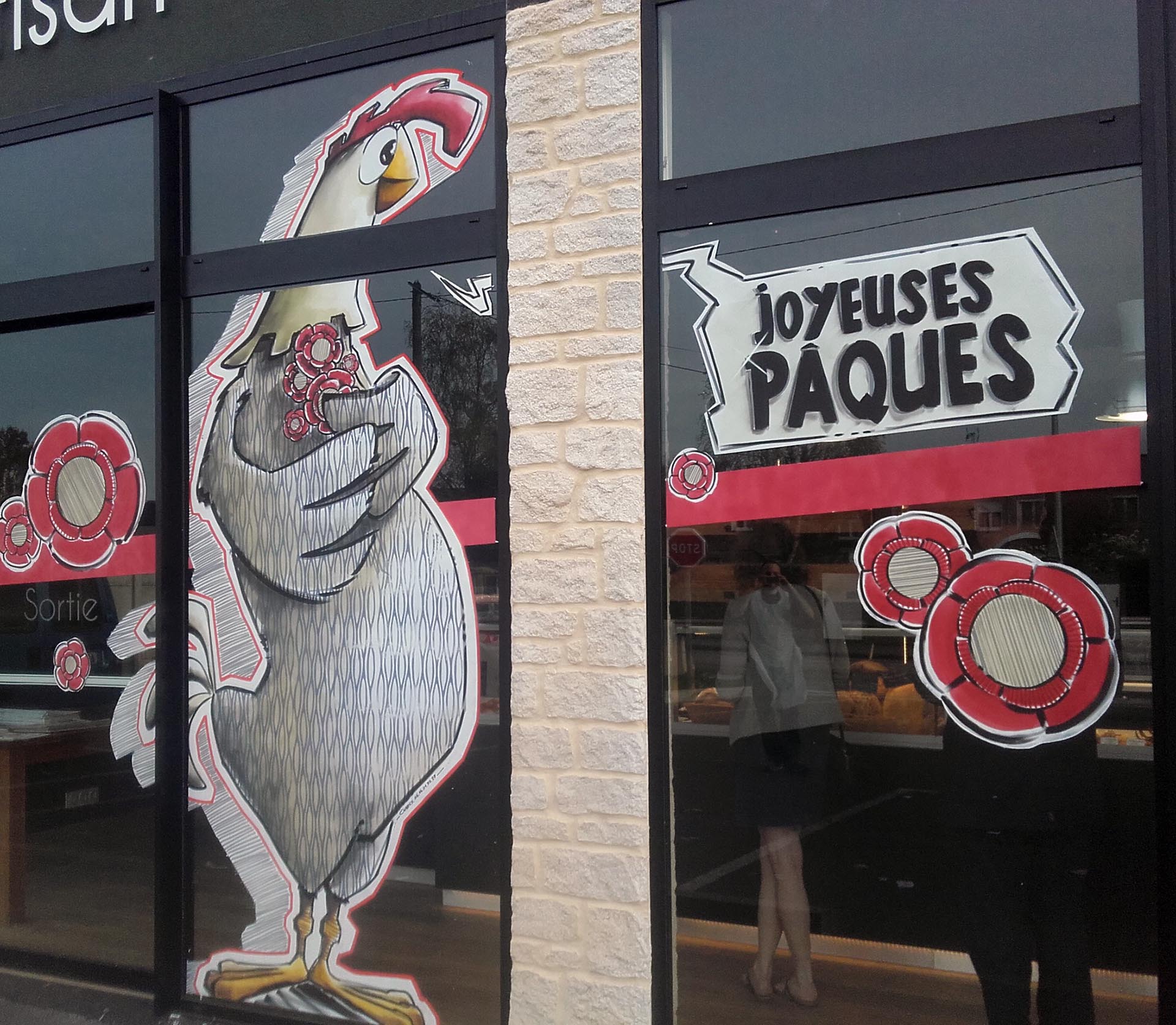 Peinture sur vitrine de Pâques par Jean‑Charles Varlet, poule stylisée et fleurs rouges.